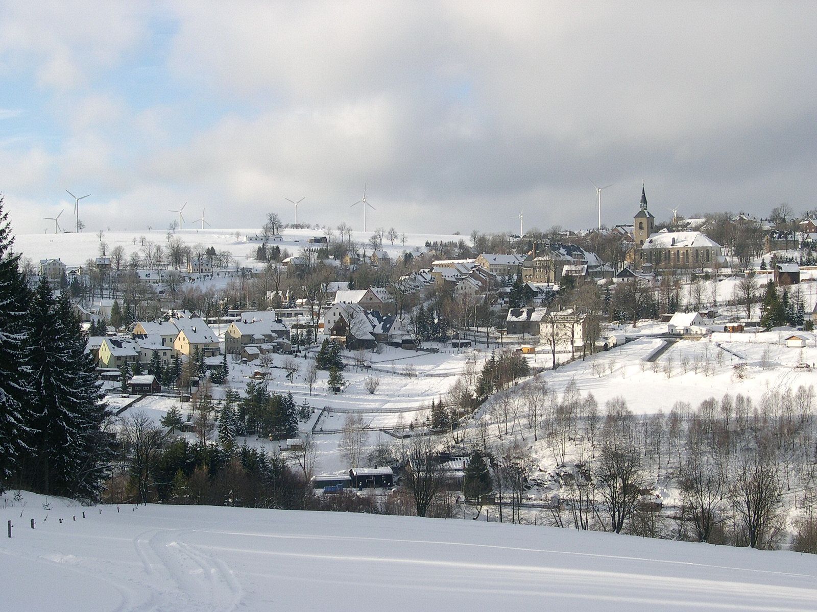 Blick auf die schneebedeckte Kulisse der Bergstadt Jöhstadt mit Lokschuppen im unteren Bilddrittel und St. Salvator-Kirche in der Bildmitte