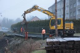 Mit dem Bagger werden neue längere Schienenstücke in den Hang gedrückt. Die neue Bahnsteigbegrenzung mit Holzschwellen liegt noch im Vordergrund gestapelt.