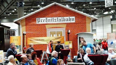 Das Messezelt der Preßnitztalbahn, dem Stationsgebäude von Schmalzgrube nachempfunden, wurde auf dem Messestand wieder als Materiallager verwendet, vor dem ein Präsentationsbereich für Videos der Schmalspurbahnen aufgebaut war.