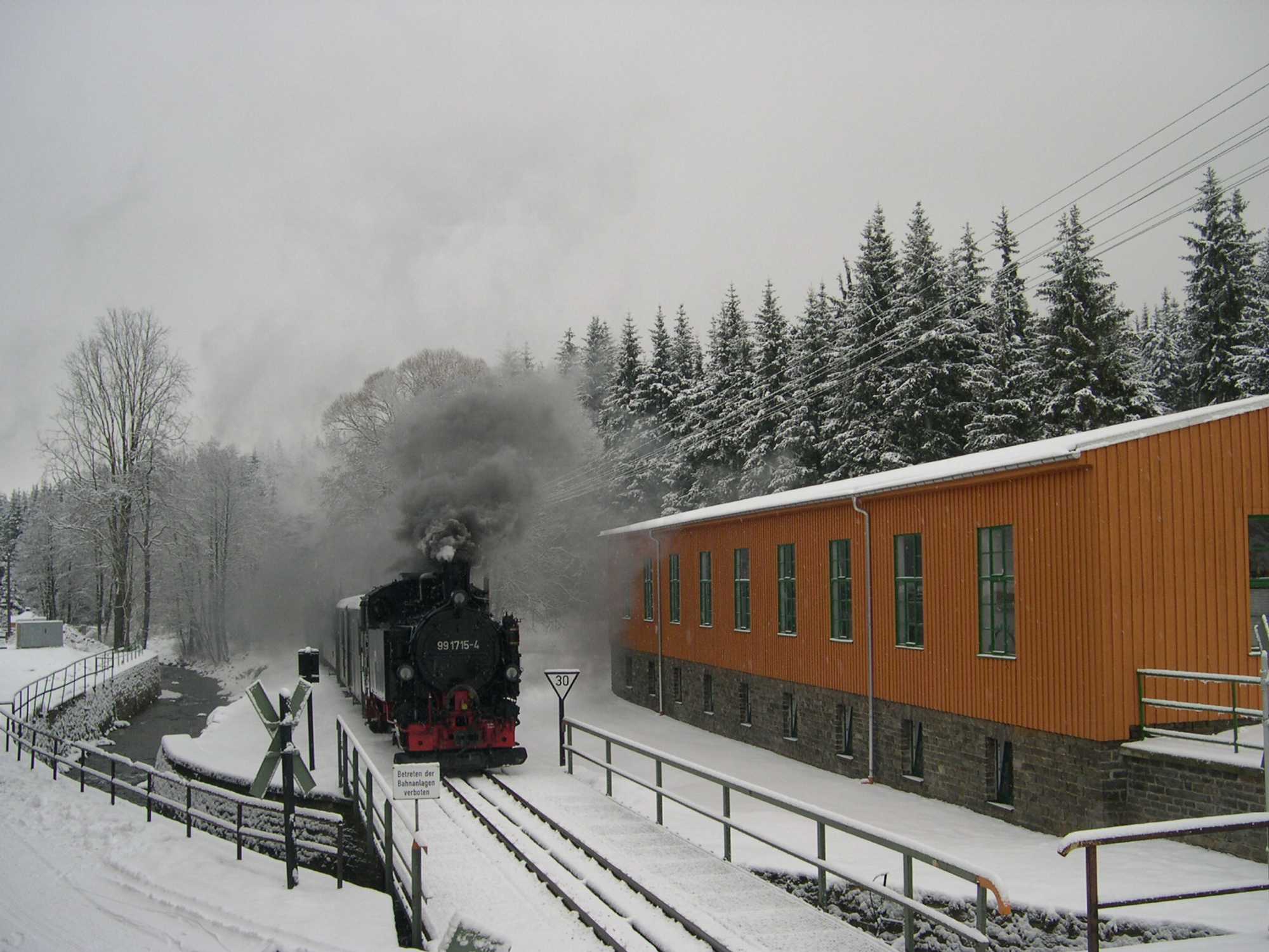 Ein Zug mit der VI K 99 1715 passiert die Lagerhalle in Schlössel.
