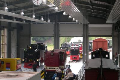 Am Sonnabend Vormittag passiert 99 4511 mit ihrem Pendelzug zwischen Bahnhof Jöhstadt und Bahnhof Schlössel die Ausstellungs- und Fahrzeughalle mit den darin und davor abgestellten Fahrzeugen.