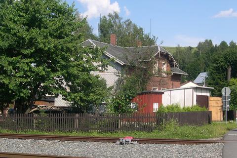 Von der Gleisseite des Bahnhofes Steinbach ist das Gebäude kaum zu erkennen, da ein großer Kirschbaum sowie eine Gartenlaube und eine Garage die Sicht verdeckt. Die gleisseitige Stirnseite ist mit einer Schindeleindeckung versehen. | 18.07.2004 | Foto: Jörg Müller Von der Gleisseite des Bahnhofes Steinbach ist das Gebäude kaum zu erkennen, da ein großer Kirschbaum sowie eine Gartenlaube und eine Garage die Sicht verdeckt. Die gleisseitige Stirnseite ist mit einer Schindeleindeckung versehen.
