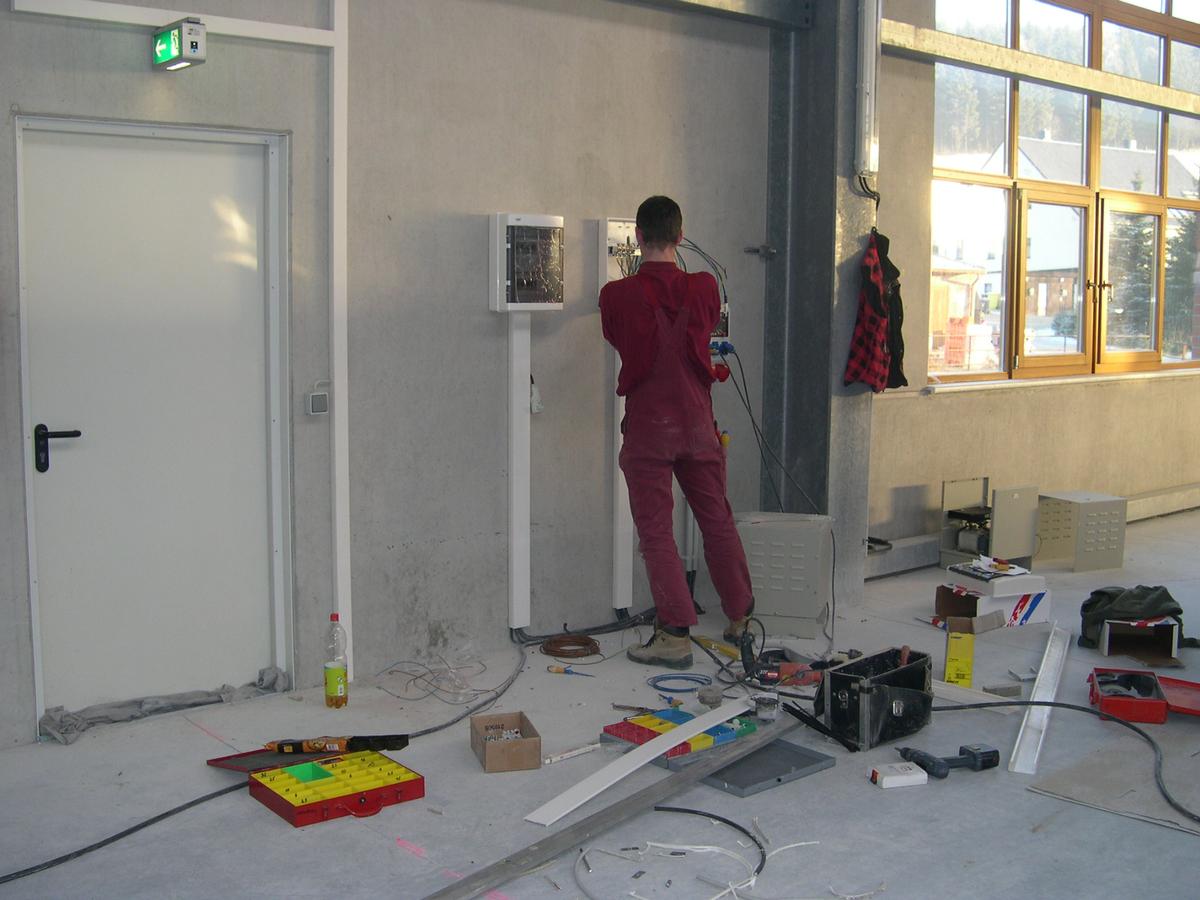 Installation der Sicherungs- und Schaltkästen der Niederspannungstrafos an der Hallenwand durch den Elektriker.