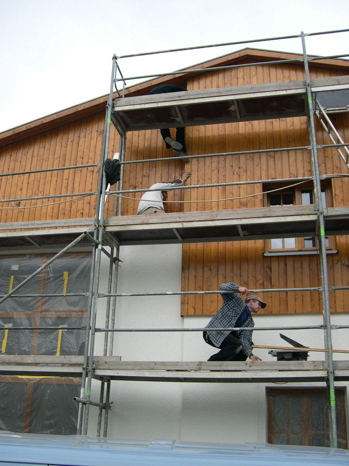 An der Giebelfassade des Mehrzweckgebäudes werden die letzten Holzlatten montiert.